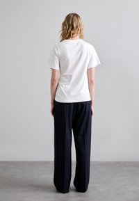 Bílý bavlněný tričko s krátkým rukávem, doplněné volnými černými kalhotami. Tento outfit je jednoduchý, bez vzorů nebo viditelného hardwaru.