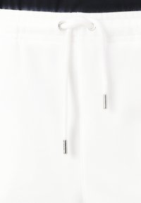 Witte sweatpants hebben een tailleband met trekkoord met zilveren hardware, een gladde textuur en een eenvoudig, strak ontwerp.