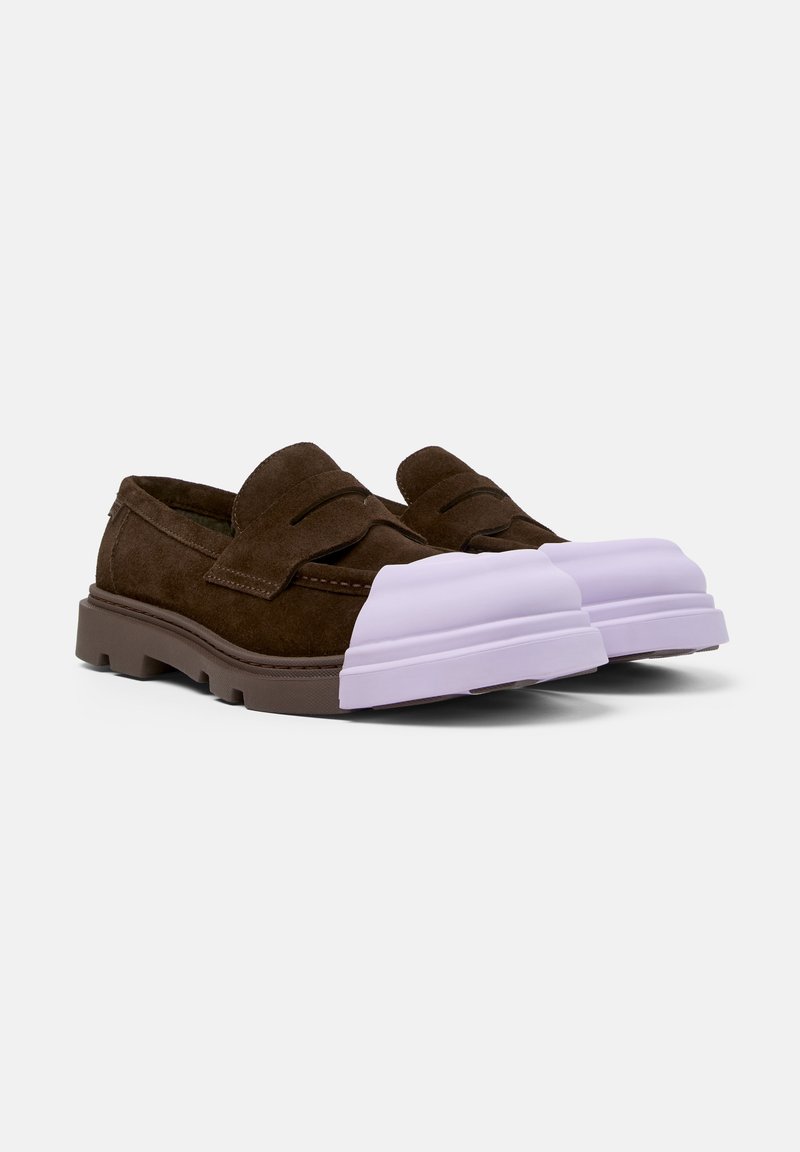 Des chaussures slip-on en suede marron avec un épais capuchon en caoutchouc lilas à l'avant et des semelles texturées marron. Le design inclut une bande en cuir cousue sur le dessus.
