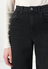 Black high-waisted jeans with a classic five-pocket design, featuring a button and zip closure, and subtle stitching details.