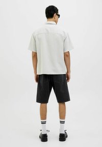 Camiseta corta de manga corta en gris claro, con tela texturizada, combinada con pantalones cortos de mezclilla negros, de color sólido, hasta la rodilla, y zapatos negros con calcetines blancos hasta el tobillo.