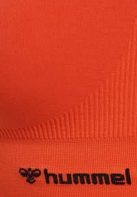 Jaskrawo pomarańczowa tkanina sportowa o żebrowej teksturze, z czarnym logo na dole. Materiał o wysokiej elastyczności, idealny do odzieży sportowej.