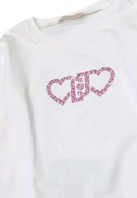T-shirt bianco in cotone con design a cuore in strass rosa e testo stilizzato tra i cuori. Maniche corte e scollatura rotonda.
