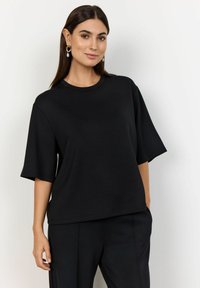 Tricou negru cu mânecă scurtă, realizat dintr-un material neted, având un decolteu rotund și o croială supradimensionată, purtat cu pantaloni negri asortați.
