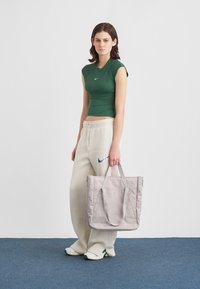 Szürke nylon bevásárlótáska, dupla vállpántokkal, sima tapintással és cipzáros záródással. Zöld, fitted pólóval és bézs melegítőnadrággal viselve.