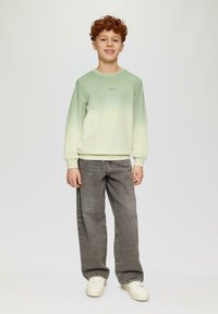 Lichtgroene sweatshirt met een gradient vervaging, ribgebreide manchetten en een klein logo. Gekleed met grijze wijde jeans en witte sneakers.