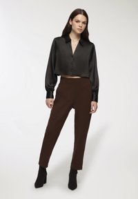 Czarna satynowa skrócona koszula z zapięciem na guziki, zestawiona z brązowymi dopasowanymi spodniami i czarnymi botkami na obcasie. Gładkie faktury i zorganizowany design.