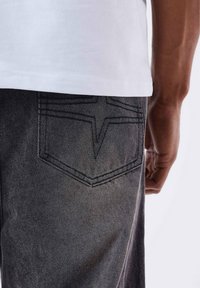 I jeans di denim neri presentano una particolare cucitura a forma di stella sulla tasca posteriore. Abbinati a una t-shirt bianca semplice.