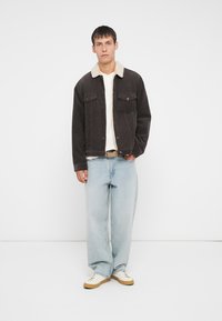 Pruunist korduroyst jack, millel on valge kunstkarvast krae, kaks rinna taskut, kantud üle valge särke ja helesiniste teksadega. Tan värvi spordijalatsid lõpetavad look.