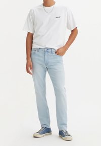 Męski casualowy strój z białą koszulką Levi's i jasnoniebieskimi dżinsami. Dżinsy mają klasyczny krój z pięcioma kieszeniami i zapięciem na guzik.