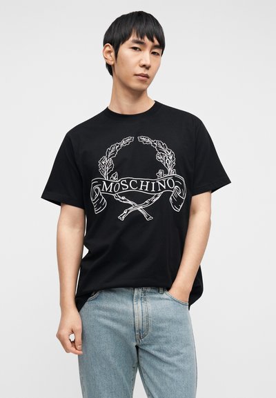 Μαύρο βαμβακερό T-shirt με λευκό γραφικό σχέδιο που απεικονίζει στεφάνι δάφνης και το κείμενο "MOSCHINO", στρογγυλή λαιμόκοψη και άνετη εφαρμογή.