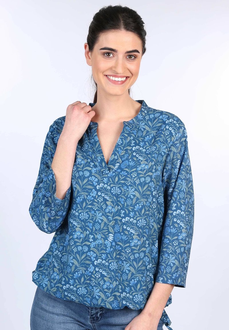 Blaue Blumenbluse mit V-Ausschnitt, 3/4-Ärmeln und lockerer Passform. Der Stoff zeigt ein botanisches Muster in verschiedenen Blautönen und Grüntönen.