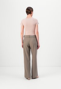 Helle beigefarbene, figurbetonte Bluse mit kurzen Ärmeln, kombiniert mit hochtaillierten, weit geschnittenen taupefarbenen Hosen. Glatte Textur und minimale Details.