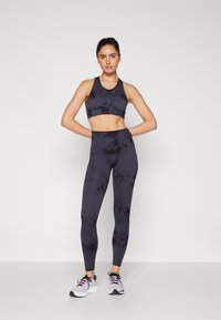 Black tie-dye sports bra and leggings set, made of stretch fabric. Designed with a fitted shape and smooth texture. Worn with sporty shoes.