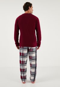 Rotes Langarmoberteil, kombiniert mit grauen und weißen Karomuster-Pyjama-Hosen. Die Hosen haben bordeauxfarbene Akzente und eine weiche Textur.