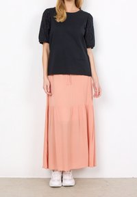 Czarna bluzka z krótkim rękawem w stylu bufek z koronką, zestawiona z lejącą się, pastelową spódnicą w kolorze brzoskwiniowym i białymi tenisówkami. Gładka tkanina, luźny krój.