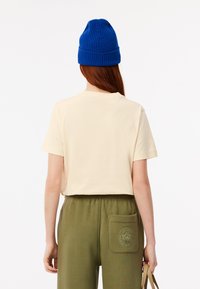 Camiseta corta de manga corta en crema, combinada con joggers verde oliva que tienen un bolsillo trasero y detalle de logo, rematada con un gorro de canalé azul.