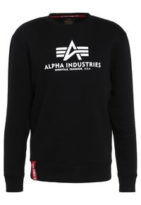 Felpa nera in misto cotone, con logo bianco "Alpha Industries" e un'etichetta rossa come dettaglio nell'orlo. Classico girocollo.
