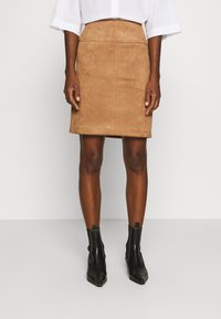 Jupe crayon en daim marron au design ajusté et texture lisse, assortie à des bottines noires à bout pointu et avec des coutures subtiles.