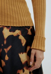 Rippene, senfgelbe Strickpulloverwärmel mit einem schwarzen und bräunlichen Rock im abstrakten Muster, der eine glatte Textur und eine figurbetonte Passform zeigt.