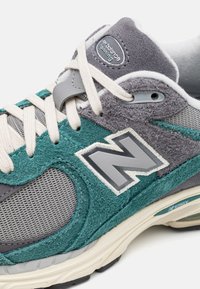 New Balance Sneaker in Teal und Grau aus Wildleder und Mesh, mit cremefarbenen Schnürsenkeln, einem grauen Logo und einer strukturierten Zwischensohle.
