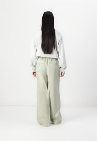 Sweatshirt gris clair à manches longues associé à un pantalon taille haute à jambes larges de couleur vert doux. Poches visibles à l'arrière du pantalon.