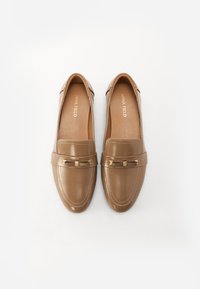 Mocassins en faux cuir marron avec un bout rond, des accents en métal doré et des détails de couture le long des côtés. Semelle plate, sans talon.