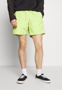 Neonově zelené šortky s elastickým pasem, bočními kapsami a drobným logem. Vypadají skvěle s černými teniskami a bílými ponožkami.