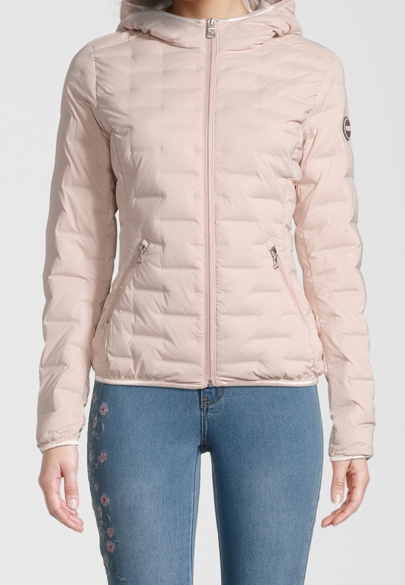 Veste matelassée rose clair, avec capuche, zip frontal et poches latérales ; présente un tissu lisse et des poignets élastiques.