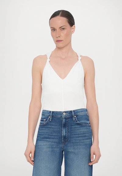 White sleeveless top with a V-neck and decorative knot straps, paired with high-waisted blue denim jeans featuring a classic cut.
