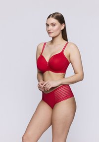 Completo di reggiseno rosso e mutandine a vita alta. Il reggiseno ha coppe lisce e dettagli in pizzo. Le mutandine presentano pannelli laterali in pizzo e una parte anteriore rossa uniforme.
