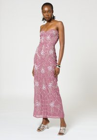 Trägerloses, figurbetontes Abendkleid aus zartem rosa Chiffon, verziert mit weißen Blumenstickereien und Pailletten. Silberne Riemchen-High-Heels runden das Outfit ab.