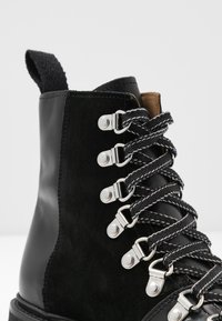 Czarne buty trekkingowe wykonane z połączenia skóry i zamszu, solidne metalowe oczka oraz czarne sznurówki z białymi przeszyciami.