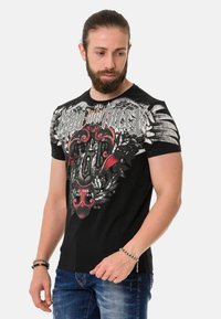 Schwarzes kurzärmliges T-Shirt mit einem grafischen Druck in Rot- und Weißtönen sowie filigranen Details, aus einem Baumwollmischgewebe gefertigt.