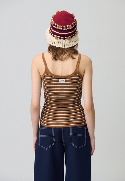 Débardeur côtelé rayé marron et blanc avec des bretelles fines, associé à un pantalon large bleu marine avec des poches arrière. Chapeau en tricot avec des accents floraux.