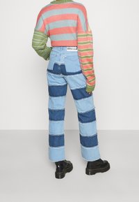 Suéter de punto a rayas con tonos verdes, rosas y azules; jeans de mezclilla de parches de talle alto en tonos azules; botas negras gruesas.