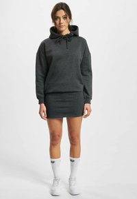 Mørkegrå hettegenser med snøring og løs passform, sammen med et grått mini-skjørt. Hvite knestrømper og hvite sneakers fullfører antrekket.