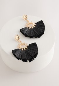 Black fan-shaped earrings made of textured material featuring a gold sunburst accent and circular centerpiece hanging from a post.