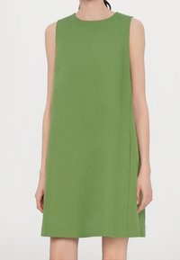 Ein ärmelloses, knielanges Kleid aus einfarbigem grünem Stoff verfügt über einen schlichten runden Ausschnitt und minimalistische Seitentaschen.