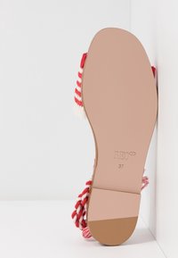 Semelle de sandale vue de dessous, beige lisse avec la taille 37 et "RED" embossé, brides tressées rouge et blanc partiellement visibles.