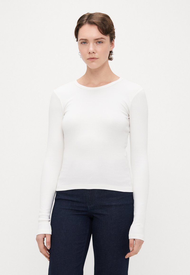 Camisola branca de mangas compridas feita de algodão canelado, com um decote redondo e silhueta ajustada. Combinada com jeans escuros.