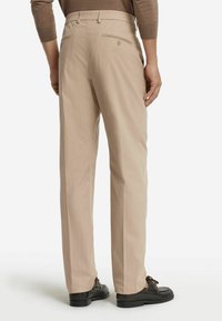 Beige skräddarsydda byxor med rak passform, utrustade med två bakfickor med knappstängning, kombinerade med svarta skor. Slät tygliknande textur.