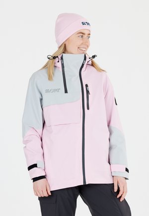 Pink und graue Skijacke mit hohem Kragen, Frontreißverschluss, Brusttasche und verstellbaren Manschetten. Getragen mit einer passenden pinken Mütze.