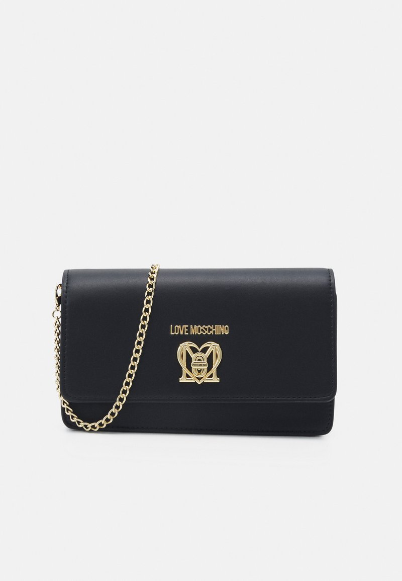 Pochette en simili cuir noir avec chaîne en métal doré, arborant un logo et un emblème à l'avant. Texture lisse et fermeture à rabat.