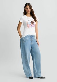 Valge puuvillane T-särk, millel on värvikas Tokyo graafika, koos helesiniste avarate denim teksade ja mustade terava ninaga kingadega.