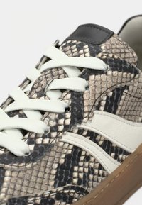 Αθλητικά παπούτσια με μοτίβο δέρματος φιδιού σε μπεζ και σκούρο καφέ αποχρώσεις, λευκές λεπτομέρειες και επίπεδες κορδόνια. Το πάνω μέρος έχει υφή και μαύρο σημείο.