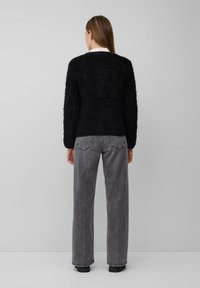 Schwarzer, strukturierten Pullover mit langen Ärmeln, kombiniert mit grauen, hoch taillierten, geraden Jeans und schwarzen Schuhen, von hinten gesehen.