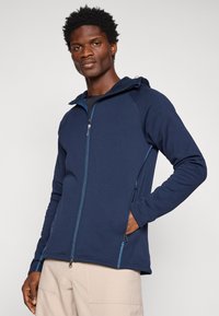 Tumesinine tõmblukuga kapuutsiga sviiter, mis on valmistatud pehmest kangast, kontrastsete õmblustega ja kahe küljetaskuga, millel on tõmblukud.