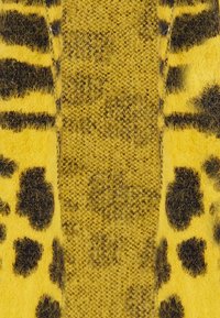 Geel textiel met een fuzzy luipaardprint in het zwart. De linkerkant heeft een gestructureerd breisel, terwijl de rechterkant een gladde, zachte stof toont.
