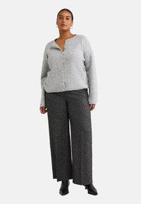 Grauer Strickcardigan mit Knopfverschluss und geripptem Struktur. Kombiniert mit weit geschnittenen, dunkelgrauen Hosen mit metallischen Einsprengseln und Ankle Boots.